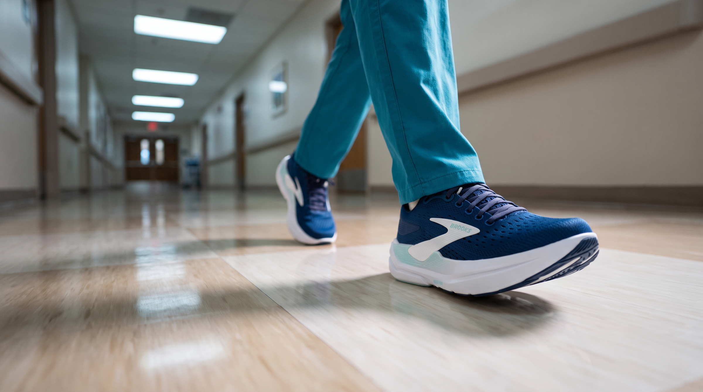 Nurse in scrubs walking down a hospital corridor wearing the Brooks Ghost Max 3, a supportive shoe for long shifts