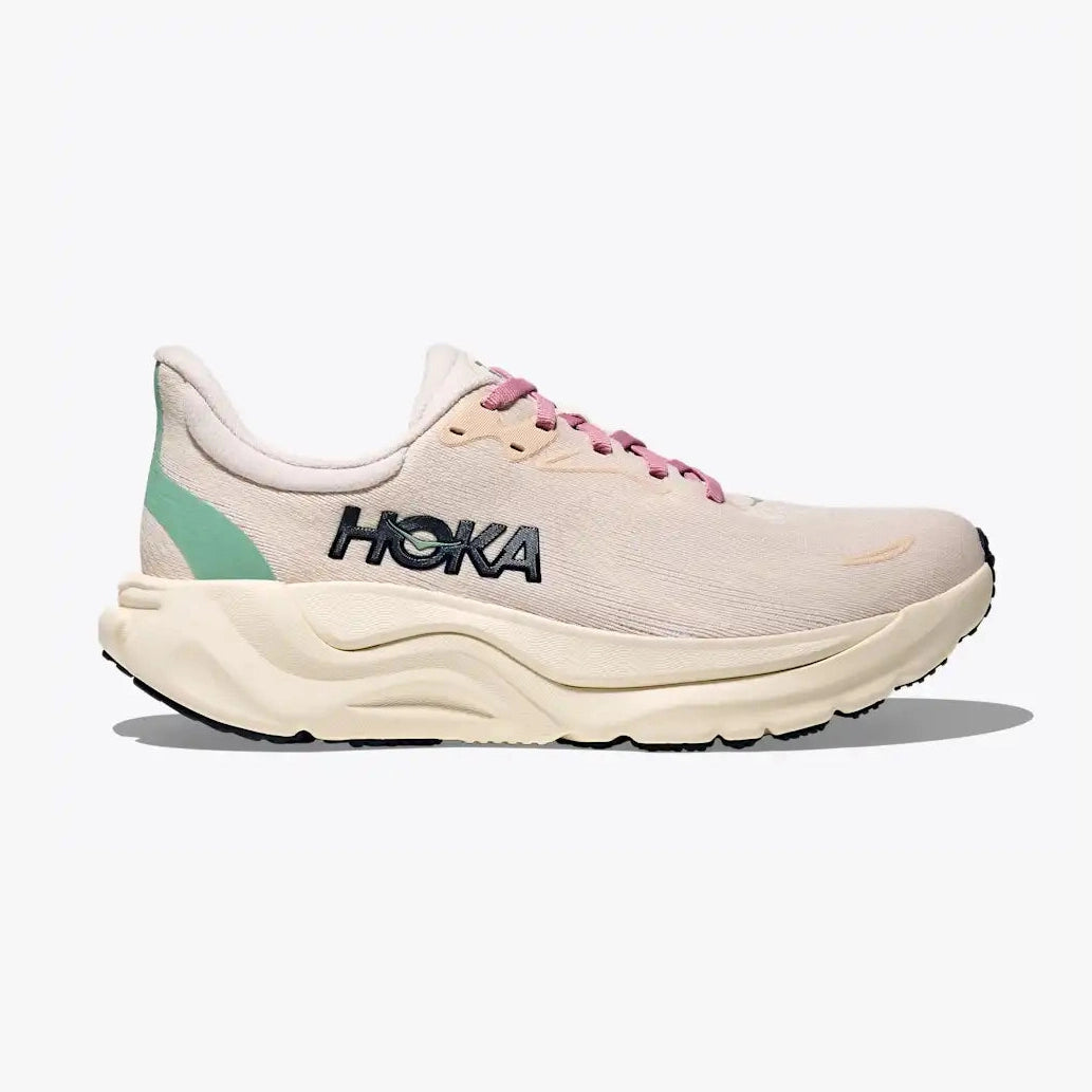A Hoka Arahi 8 – Women's running shoe in light beige with pink laces, a mint green heel accent, and a thick beige midsole, shown from a side profile on a light gray background.