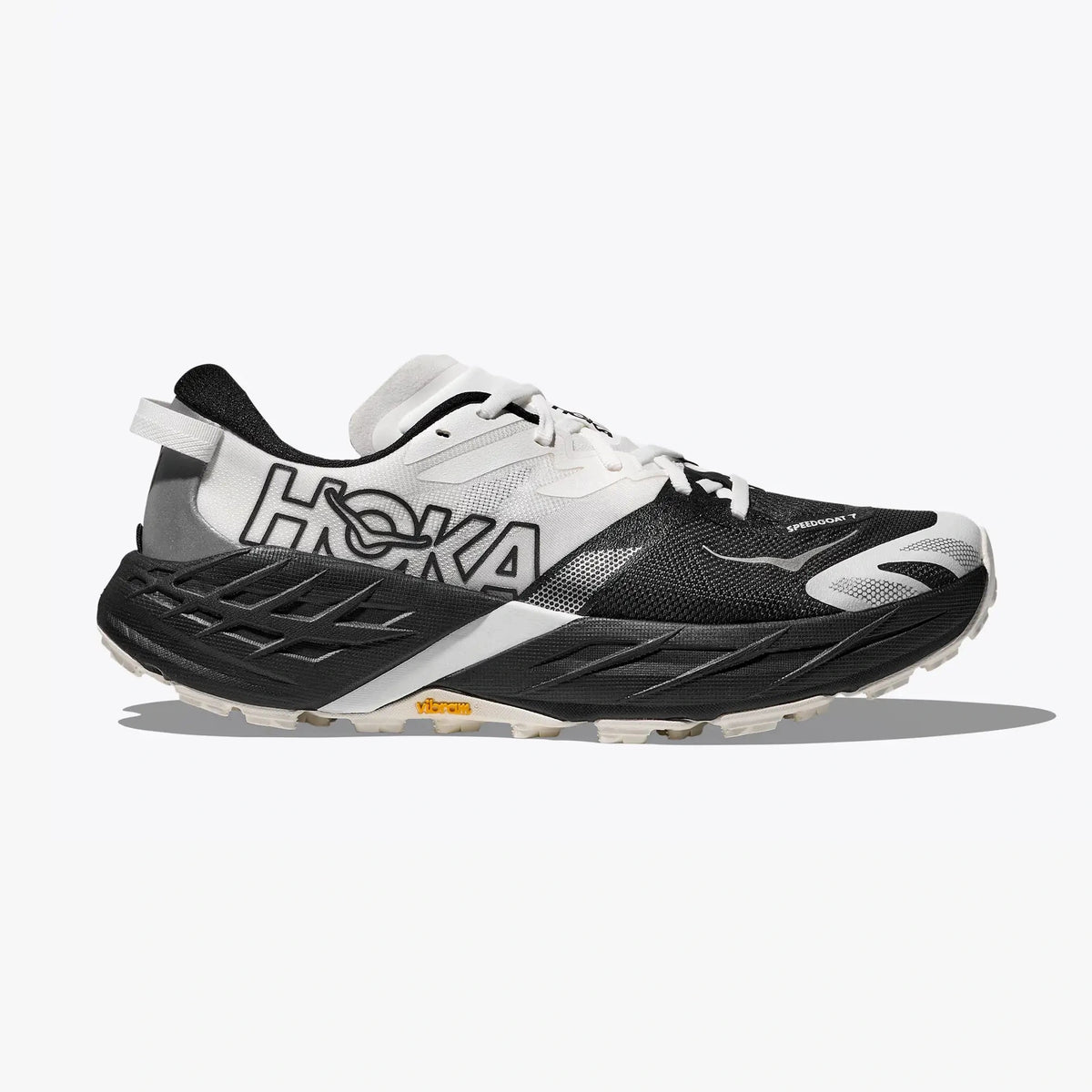 A Hoka Speedgoat 7 – Men's trail running shoe in black, white, and gray, shown from a side profile on a light gray background with a soft shadow.
