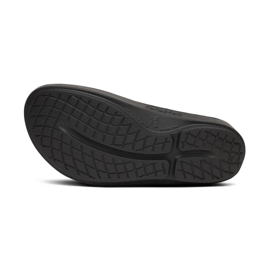 The black rubber outsole of a shoe, showing a textured tread pattern and embossed branding, photographed from a direct overhead angle on a white background.