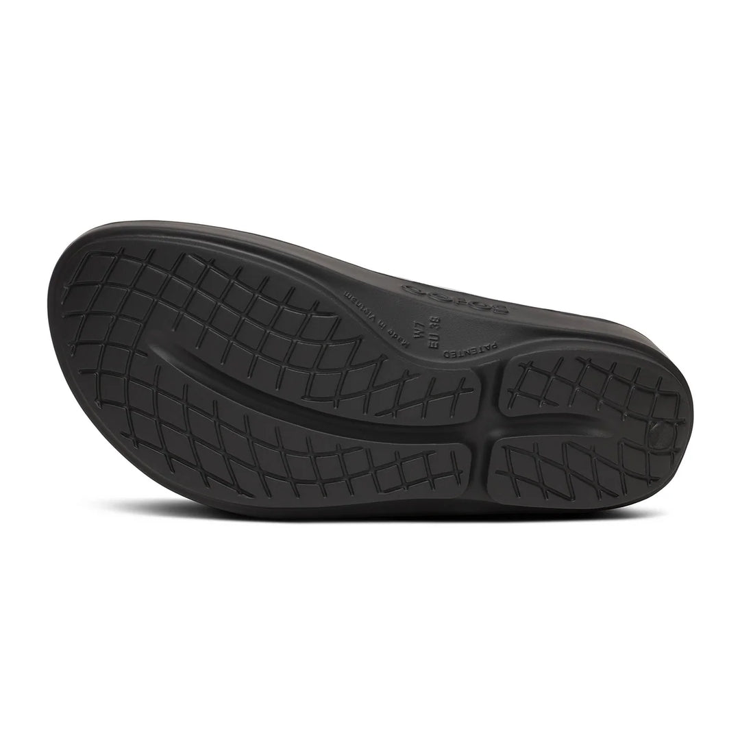 The black rubber outsole of a shoe, showing a textured tread pattern and embossed branding, photographed from a direct overhead angle on a white background.