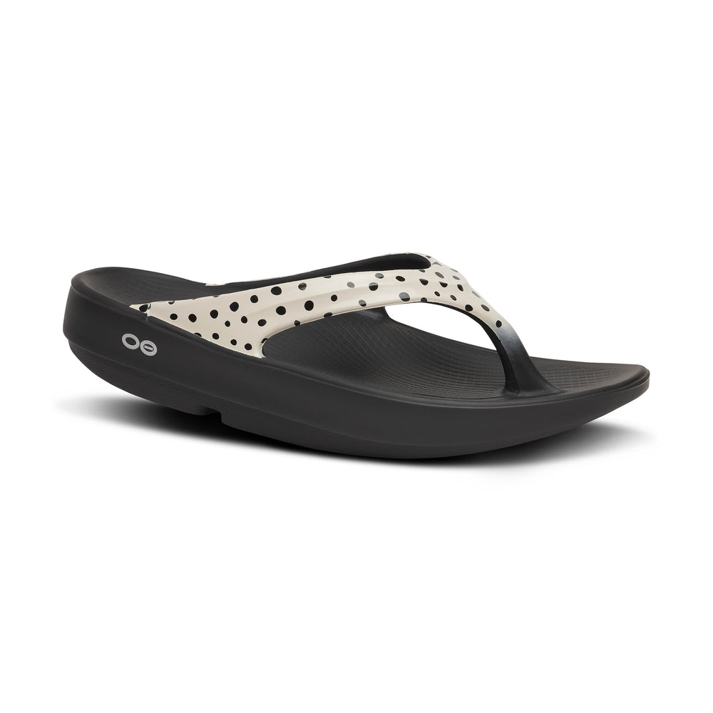 Black OOfos OOlala Limited sandal with polka dot strap on a white background