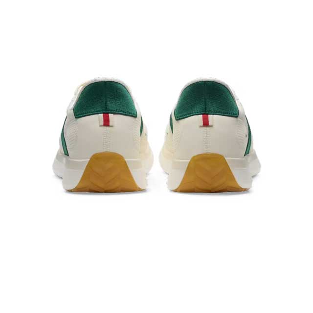 A pair of Tracksmith Eliot Ryder – All Gender low-top sneakers shown from the back, featuring an off-white leather upper, a dark green suede heel tab, a small red and green leather detail, and a textured tan rubber outsole.