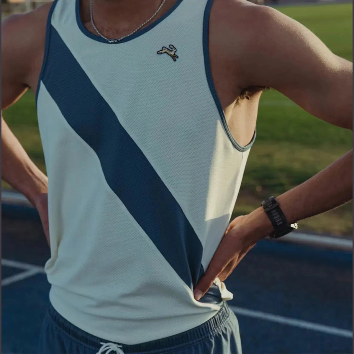 A close-up of a person wearing a Vancortlandt Singlet – Men's tank top with a diagonal navy stripe on a white background, standing on an outdoor track field.