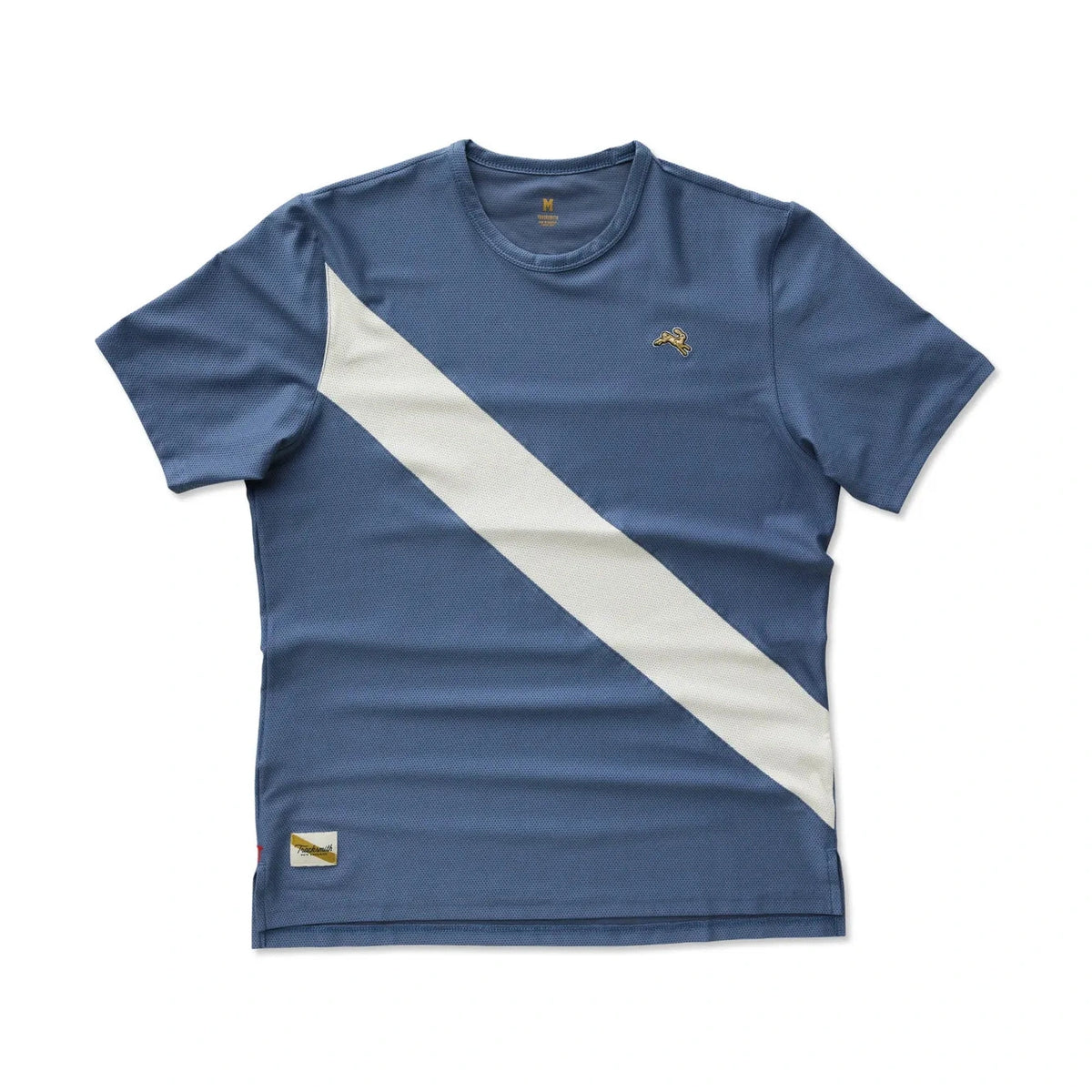 A blue Vancortlandt Tee – Men's with a bold diagonal white stripe across the chest, featuring a small gold embroidered logo on the left chest and a small gold patch near the bottom hem.
