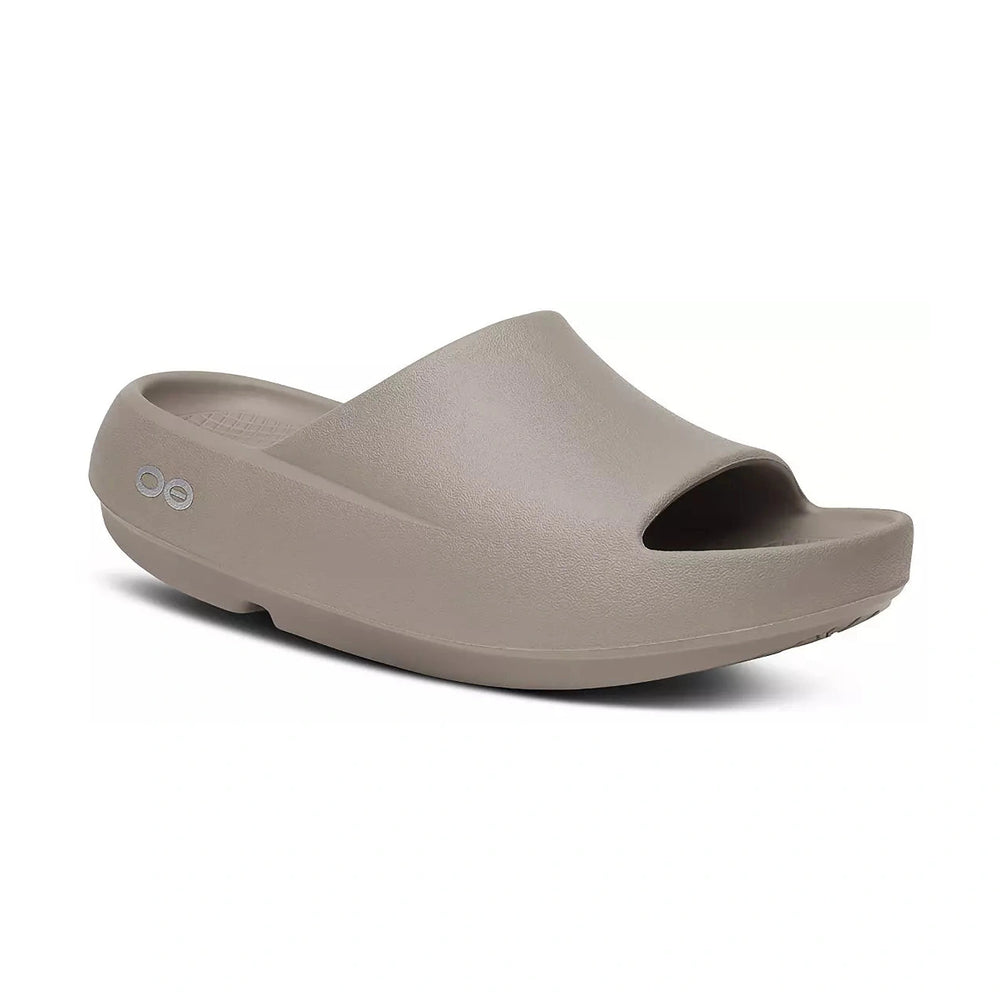 A single OOfos OOah PLUS taupe-colored slide sandal with an open toe, shown from a three-quarters angle on a white background. The brand logo 'oo' is visible on the heel.