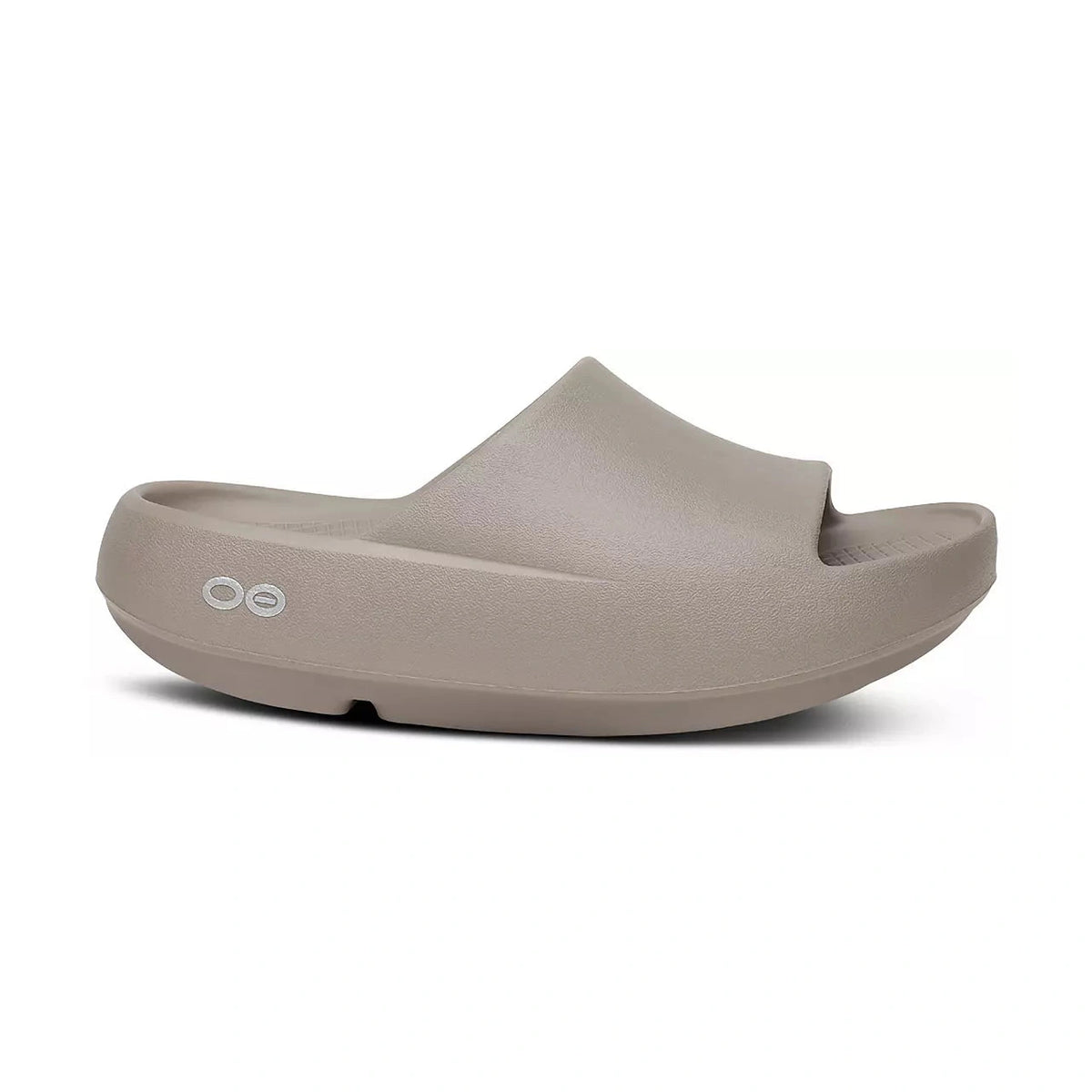 A single light taupe OOfos OOah PLUS slide sandal with a thick cushioned sole, shown from a three-quarters angle on a white background.