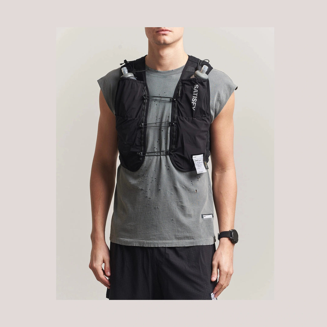 A man wearing a black Justice Cordura 5L Hydration Vest over a gray sleeveless t-shirt and black athletic shorts, shown from the neck down against a light gray studio background.