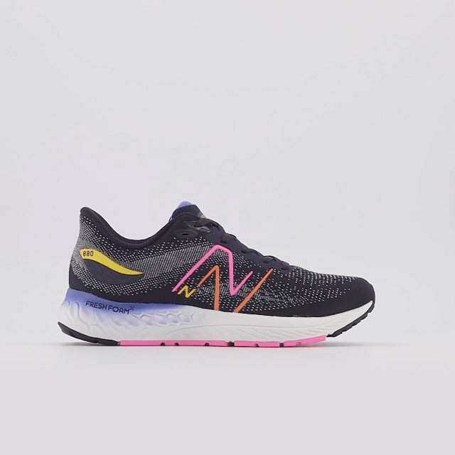 A New Balance Y 880 V12 – Kids' running shoe in black and gray with a white midsole, featuring a pink and orange 'N' logo, a yellow heel accent, and a purple and pink outsole, shown against a light gray background.