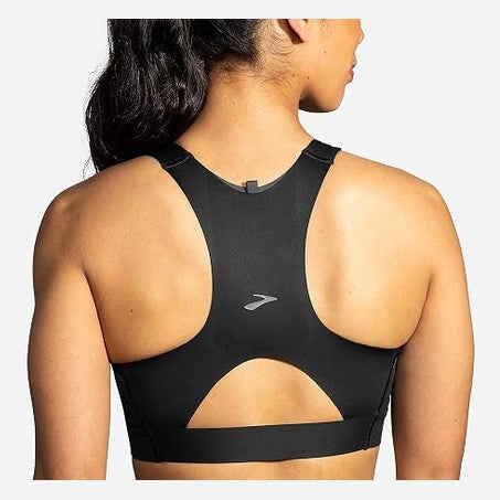 Rear view of a woman wearing a black Brooks 3 Pocket athletic sports bra with a small silver logo on the back, set against a light gray background.