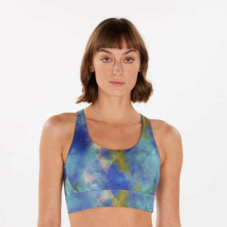 A woman modeling a matching activewear set featuring a blue, teal, and green tie-dye pattern, consisting of a Alwrld Alrn Ventilated Back Crop Bra – Women's and high-waisted leggings, against a plain white background.