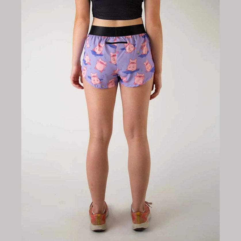 A person shown from the back wearing purple Chicknlegs 1.5" Split Shorts – Women's with a pink cartoon cat pattern, a black waistband, and pink-and-white sneakers against a plain light gray studio background.