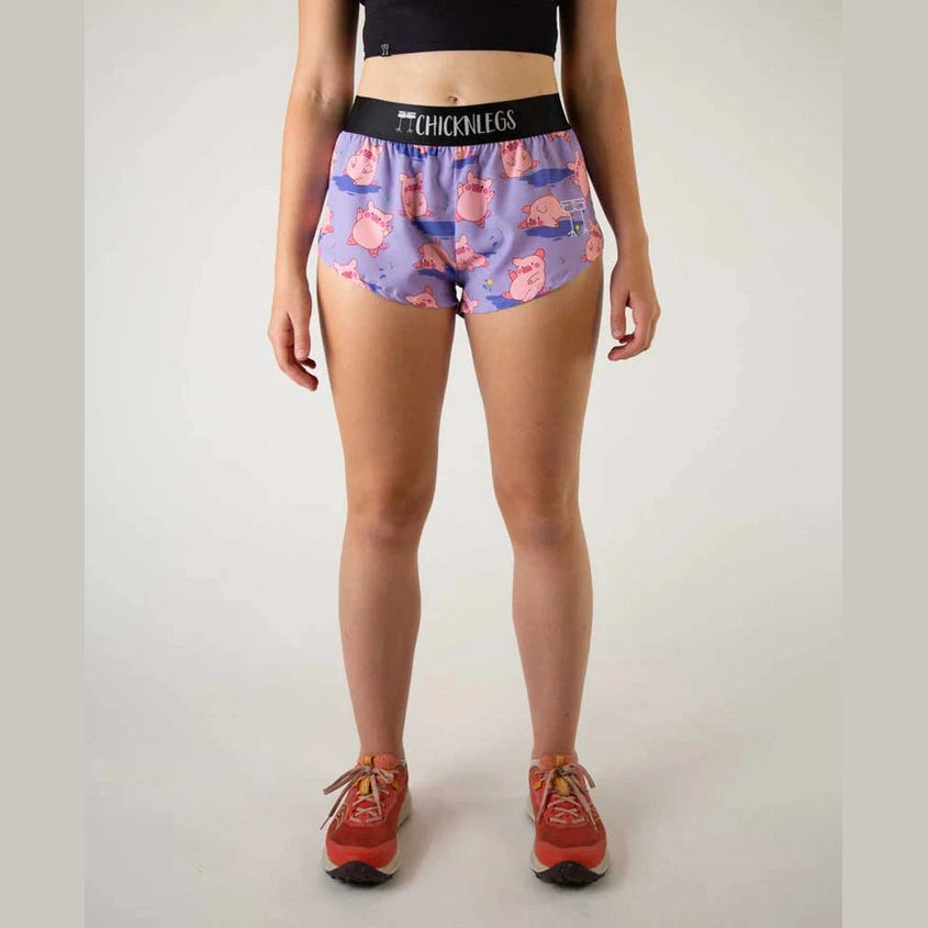 A model is shown from the waist down wearing patterned Chicknlegs 1.5" Split Shorts – Women's with a black waistband that reads 'CHICKLEGS'. The shorts feature a purple and pink cartoon chick pattern.