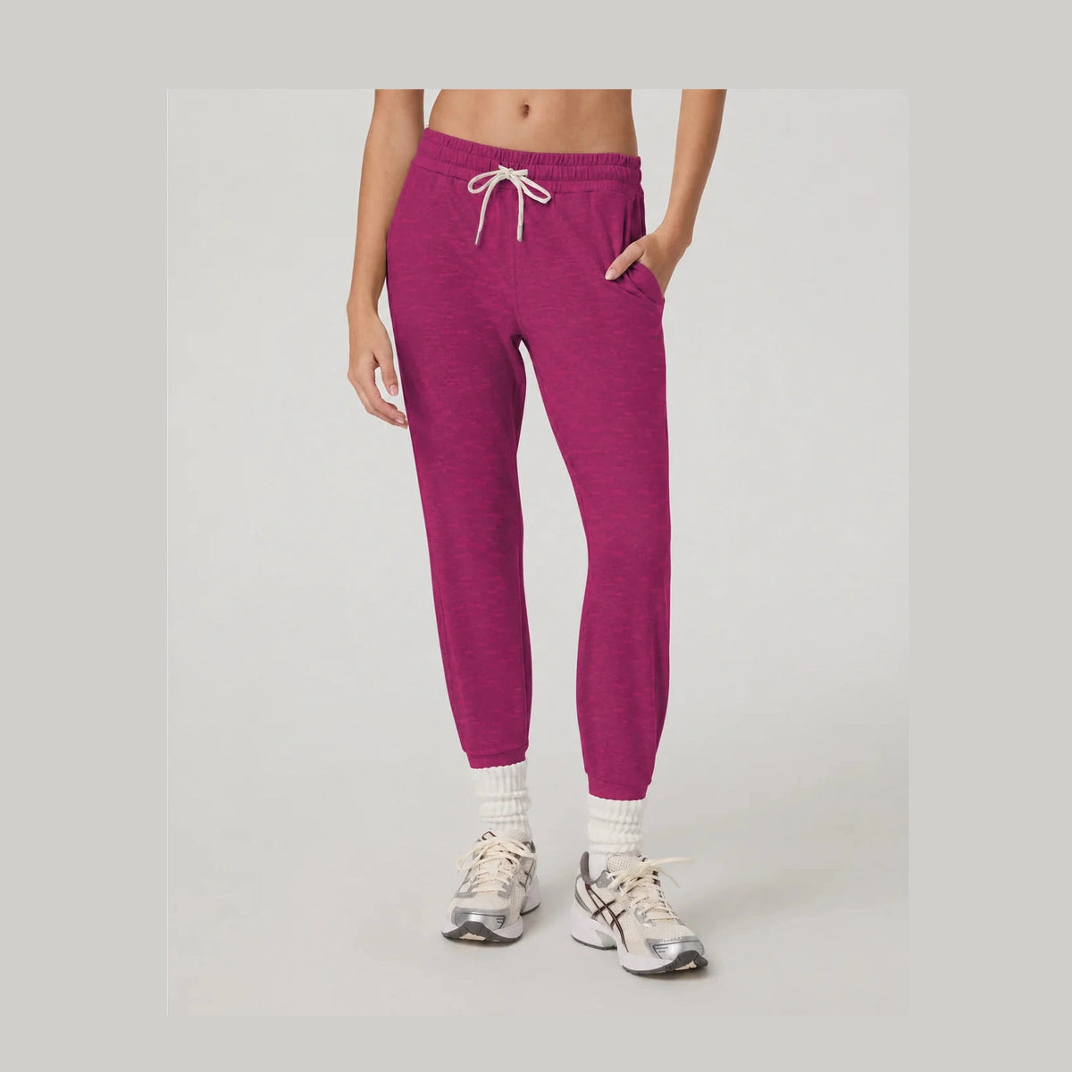 A person wearing heather magenta Performance Jogger Long – Women's jogger with a white drawstring, paired with white socks and athletic sneakers, shown from the waist down against a light gray studio background.