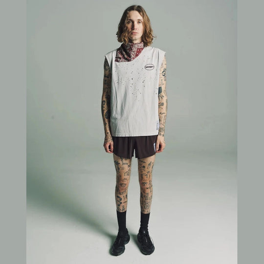 A model with tattoos stands against a light gray studio background wearing a sleeveless white vest with a small circular logo on the chest, a patterned bandana at the neck, Space-O Shorts--Men&