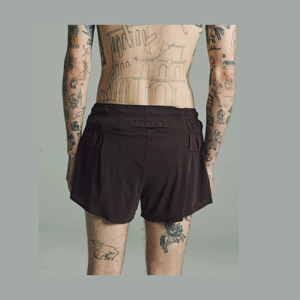 A man shown from the back wearing dark brown Space-O Shorts--Men's, with visible tattoos on his arms and legs against a plain light gray studio background.