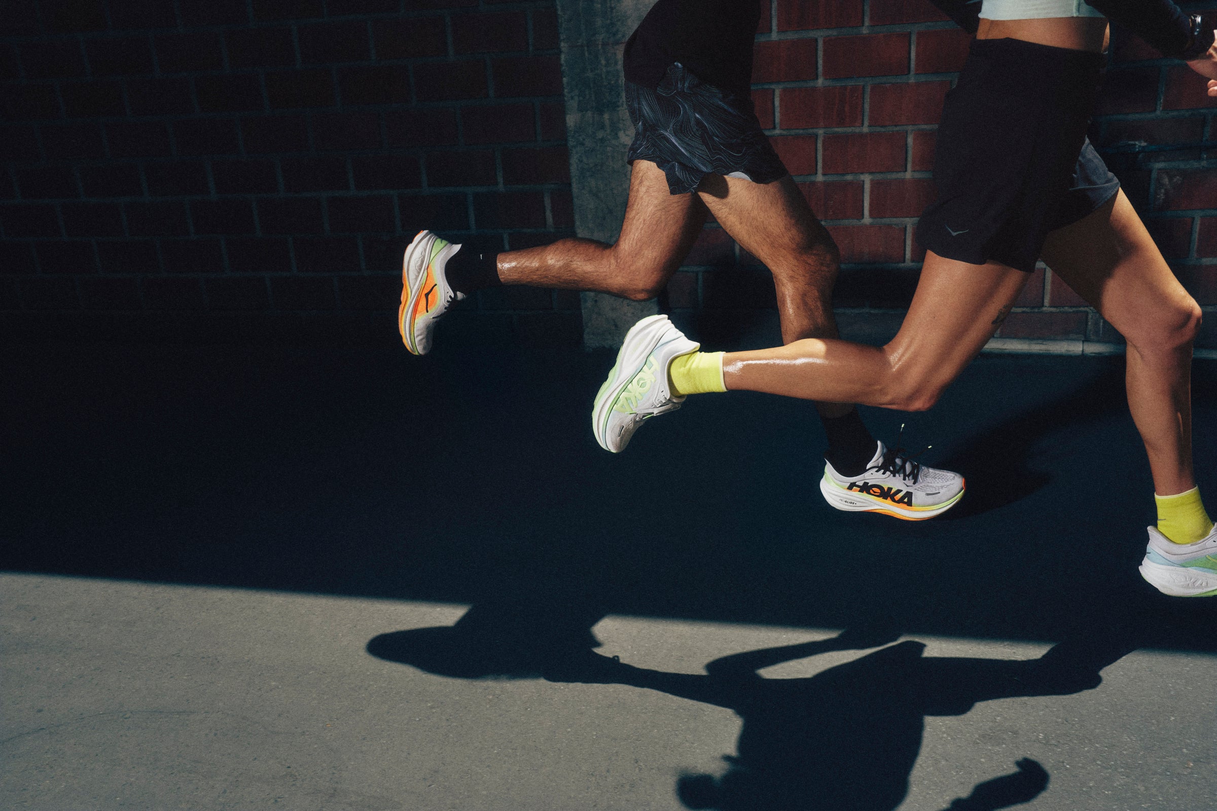 Two people running on a dark surface with a brick wall in the background