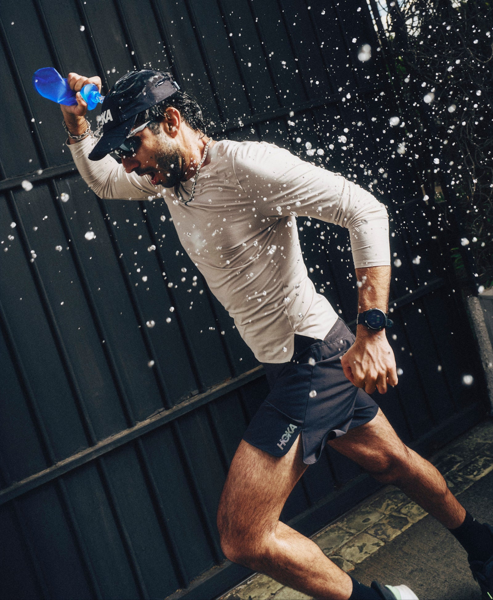 Person running outdoors with water splashing around, wearing a cap and light-colored shirt  in Hoka Clifton Pro shoes