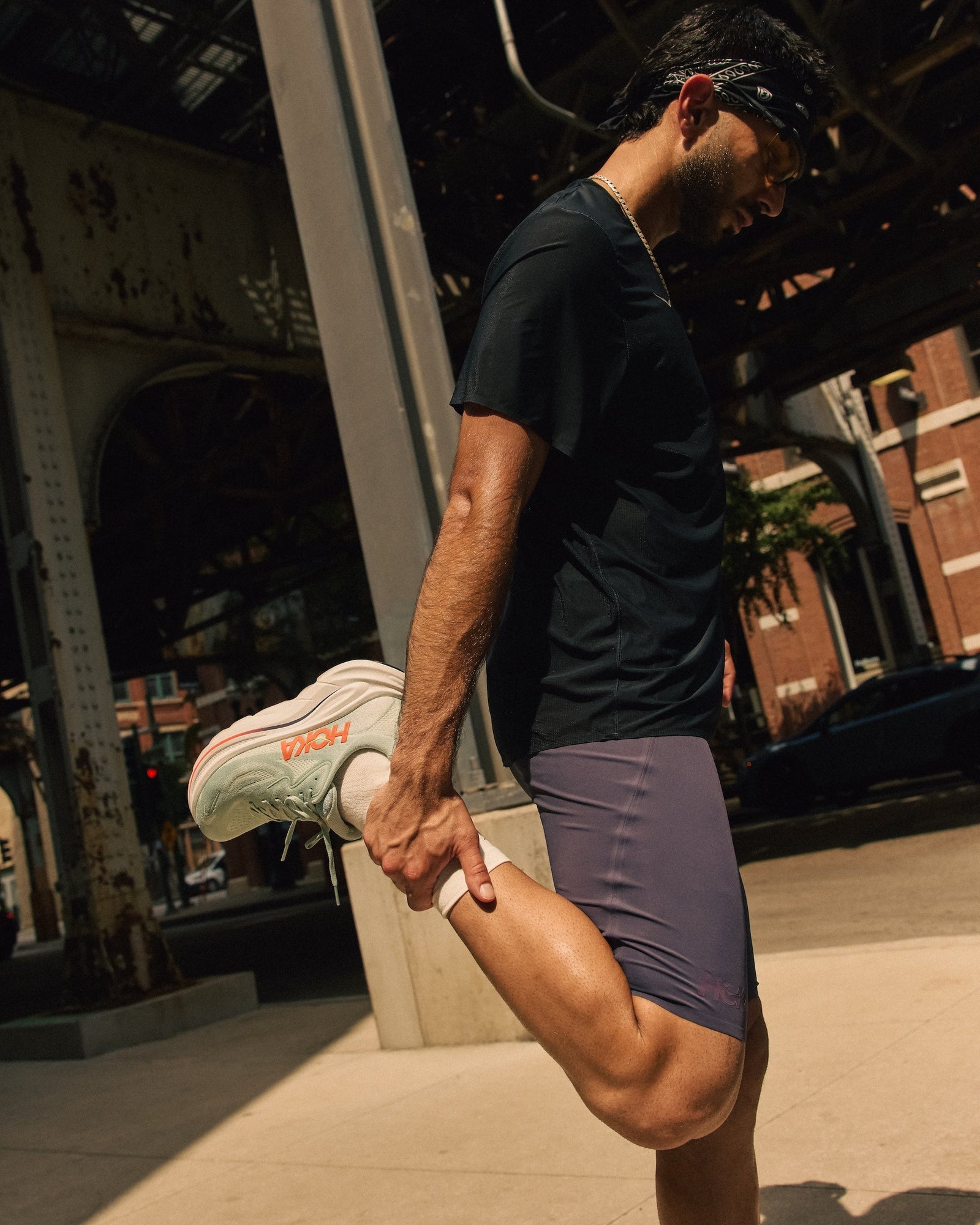 Person stretching outdoors on a city street wearing Hoka Men's Clifton 10 running shoe.