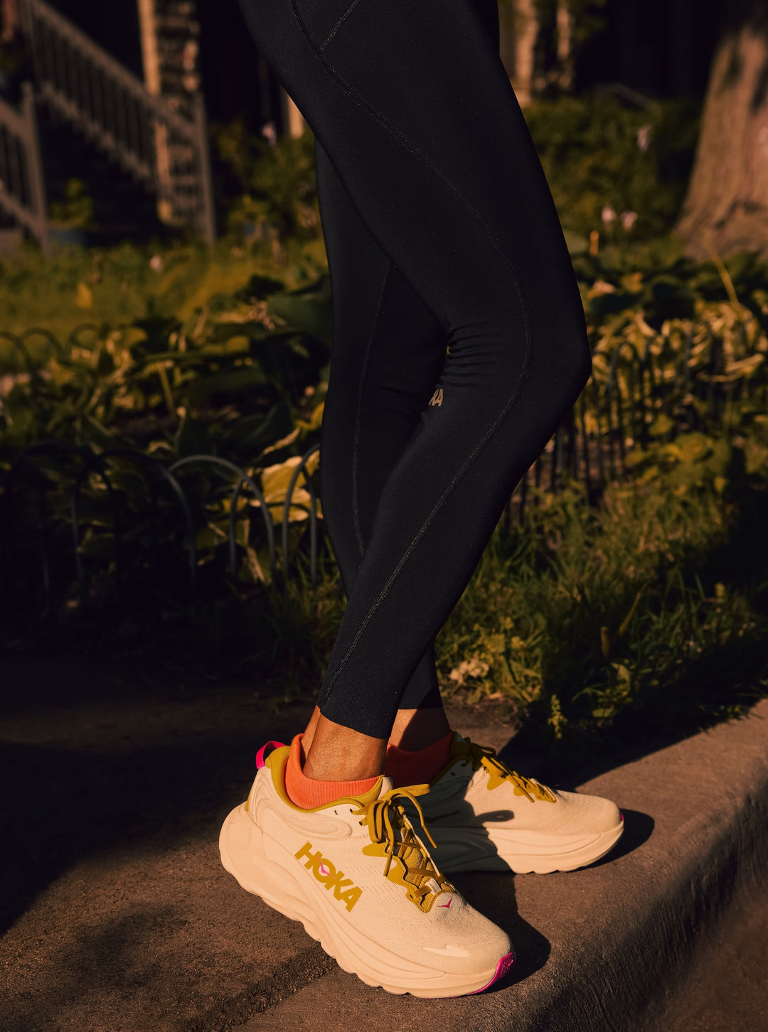 Person wearing black leggings and white Hoka Gaviota 6 sneakers with yellow accents on a stone surface.