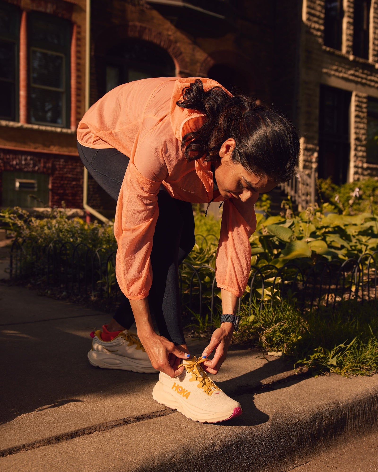 Woman tying her Hoka Gaviota 6 shoe on a sidewalk with buildings in the background