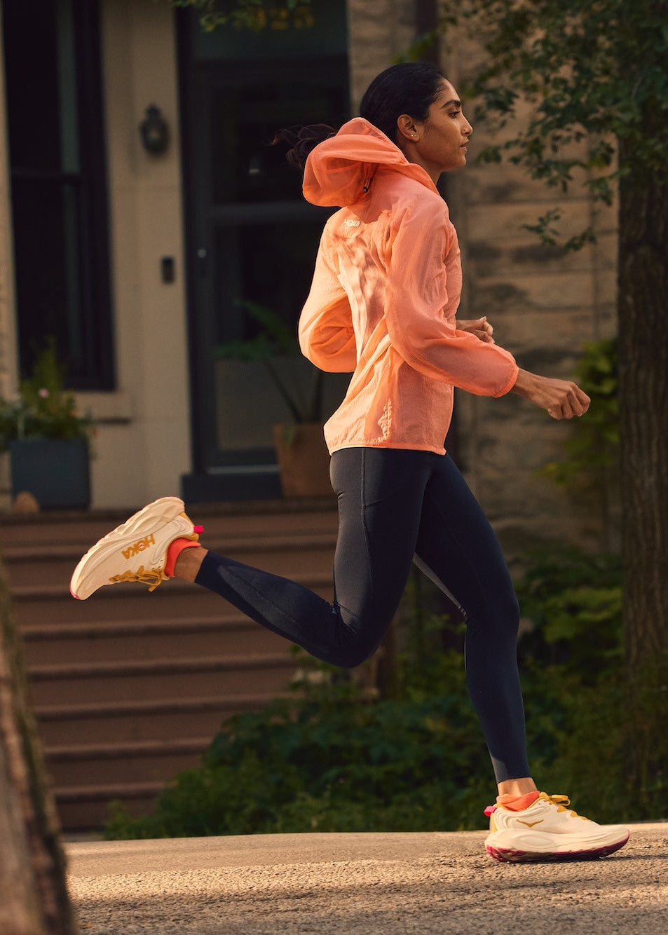 Person running outdoors in Hoka Gaviota 6 shoes on a street with trees and a building in the background
