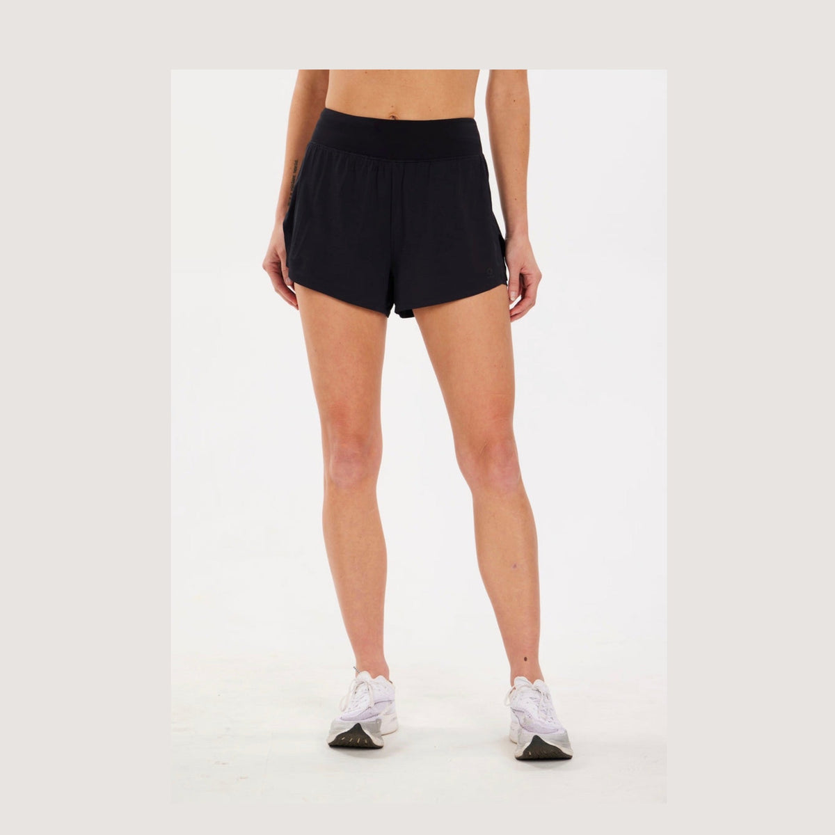 A model from the waist down wearing black Alwrld Alrn N.B.P. Mesh Short – Women's  and white sneakers, standing against a plain white studio background.