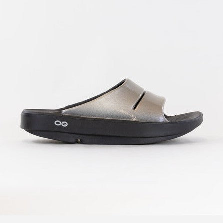 A single OOfos OOahh Luxe shown in profile against a clean white background. The upper strap is metallic silver with a subtle sheen, while the sole is black.