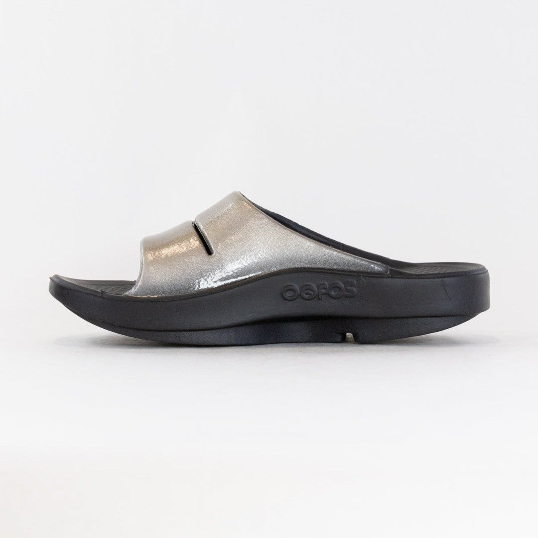 Black and silver OOfos OOahh Luxe sandal on a white background