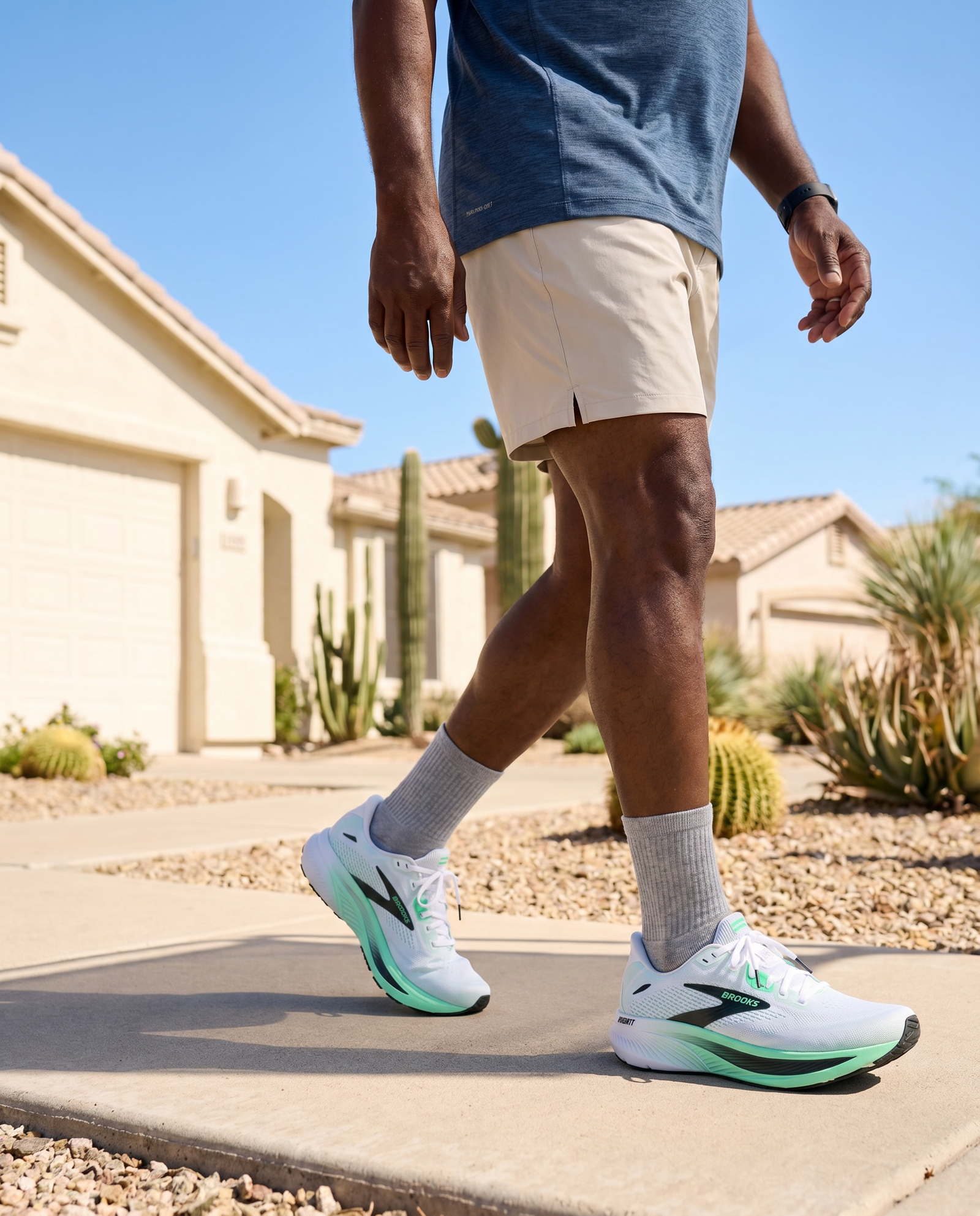 Person wearing white Brooks Ghost 18 running shoes with green accents on a sidewalk.