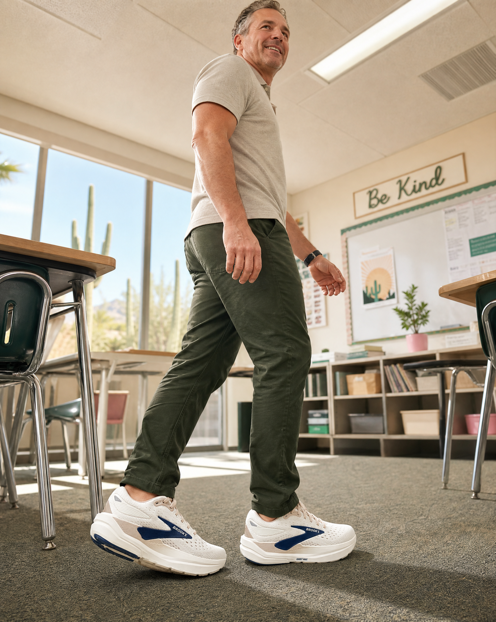 Man walking iin the Brooks Ghost Max 3 n a classroom wearing white sneakers with blue accents