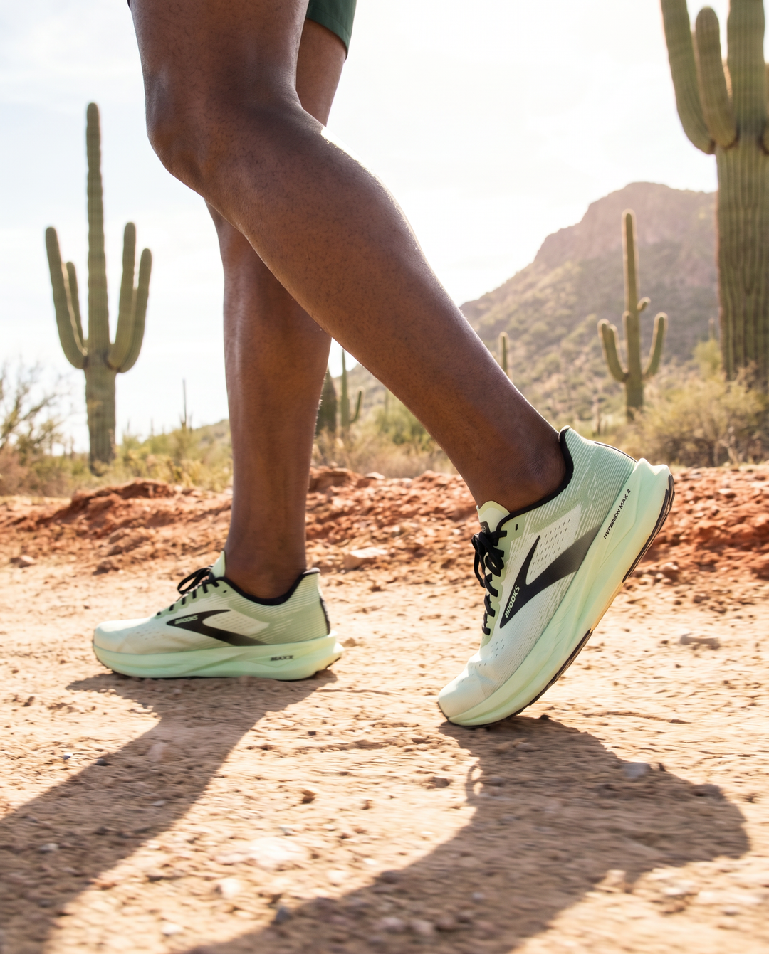 Man wearing Brooks Glycerin  23 white running shoes with black accents on a desert path with cacti in the background