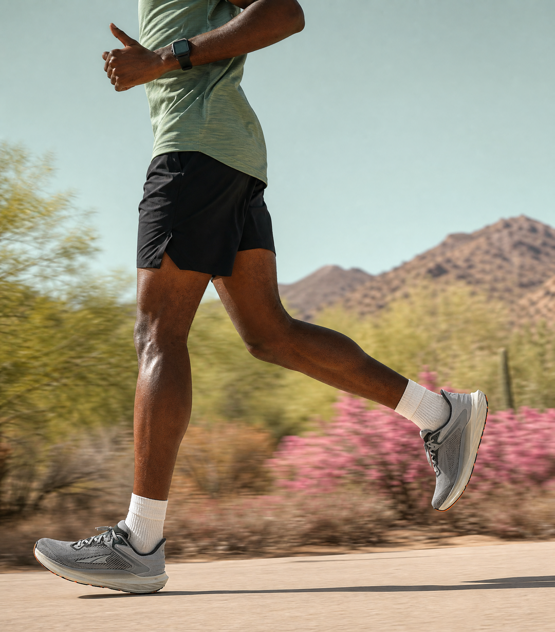 Person running on a path with mountains and pink flowers in the background