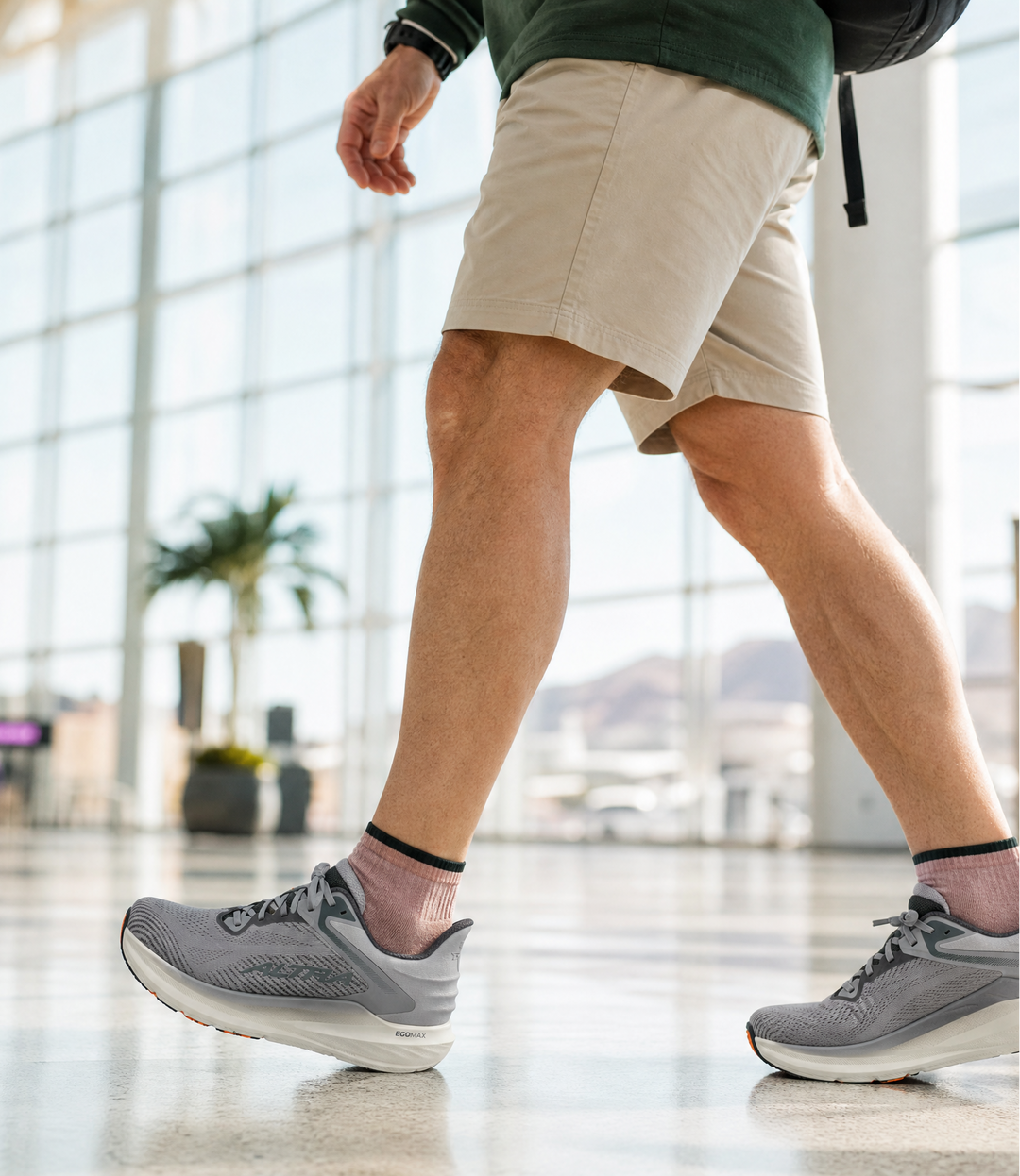 Person walking in a modern indoor setting wearing gray sneakers and beige shorts.