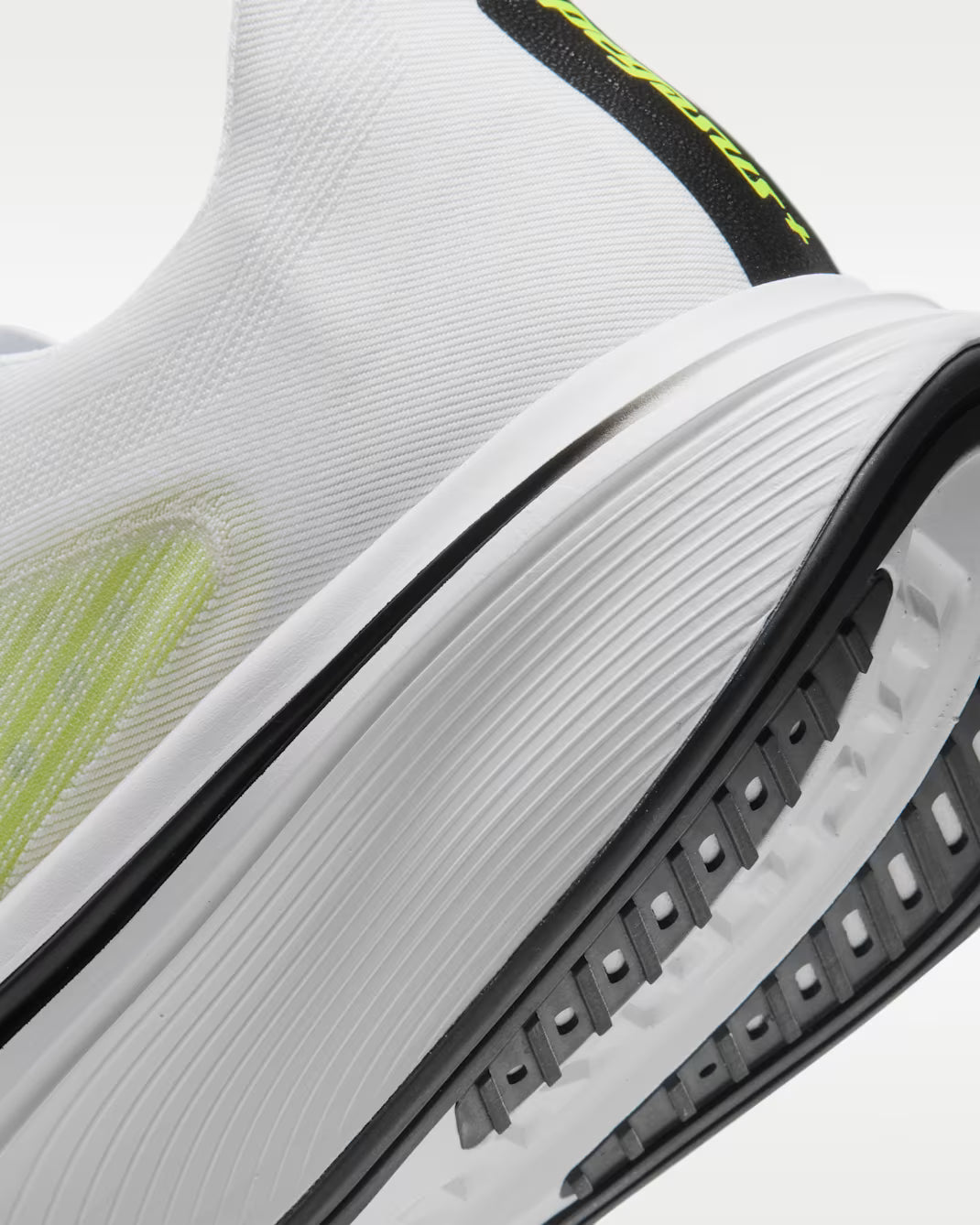 Close-up of a white athletic shoe showing the textured knit upper, thick white midsole, black outsole, and neon yellow-green accents.