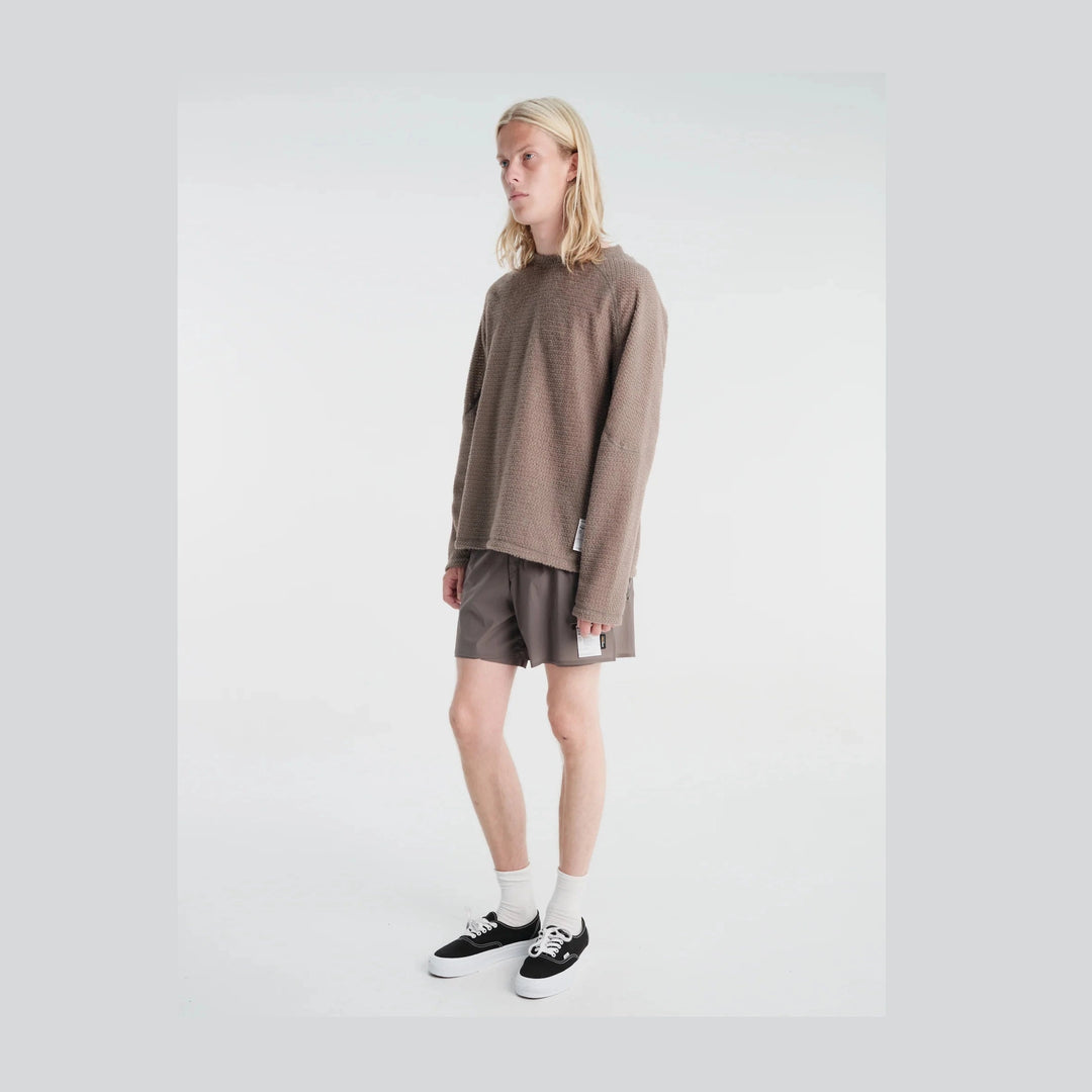 A model with long blonde hair stands in a studio wearing a textured taupe-brown Fuzz Fleece AD Long Tee--Men&