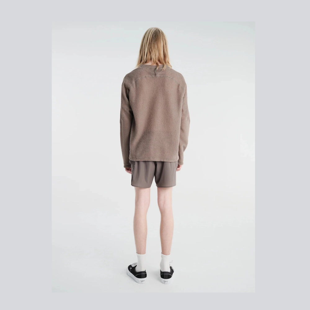 A model shown from the back wearing a textured taupe-brown long-sleeve Fuzz Fleece AD Long Tee--Men's, matching brown shorts, white socks, and black sneakers against a plain white studio background.