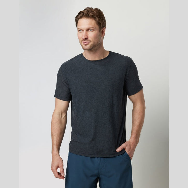Man wearing a dark gray Strato Tech Tee – Men's t-shirt and blue pants against a light gray background