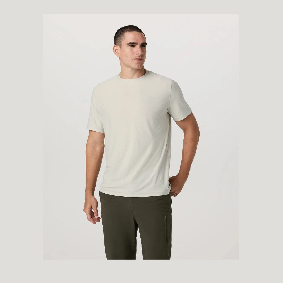 Man wearing a beige Strato Tech Tee – Men's t-shirt and green pants on a light gray background