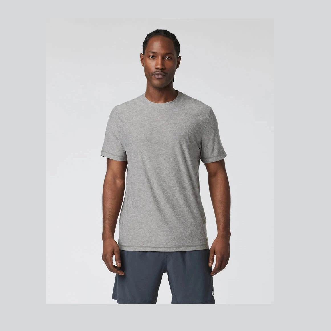 Man wearing a gray Strato Tech Tee – Men's t-shirt and dark shorts on a light gray background