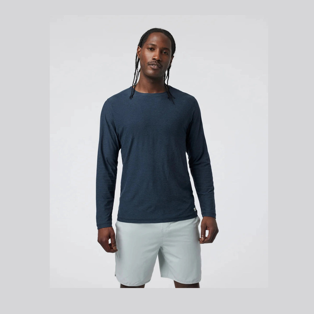 Man wearing a blue Vuori Strato Long Sleeve – Men's long-sleeve shirt and light gray shorts on a white background
