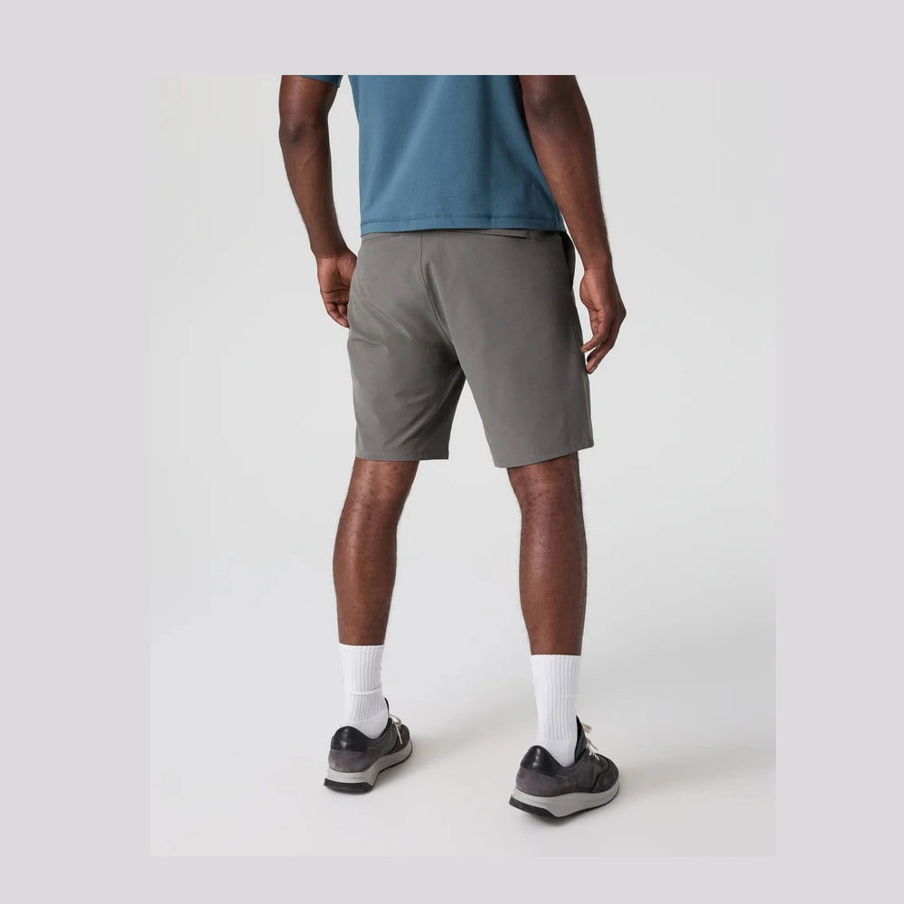 A man shown from the back wearing gray Vuori Aim Short 8" – Men's athletic shorts, a blue t-shirt, white socks, and dark running shoes against a light gray studio background.