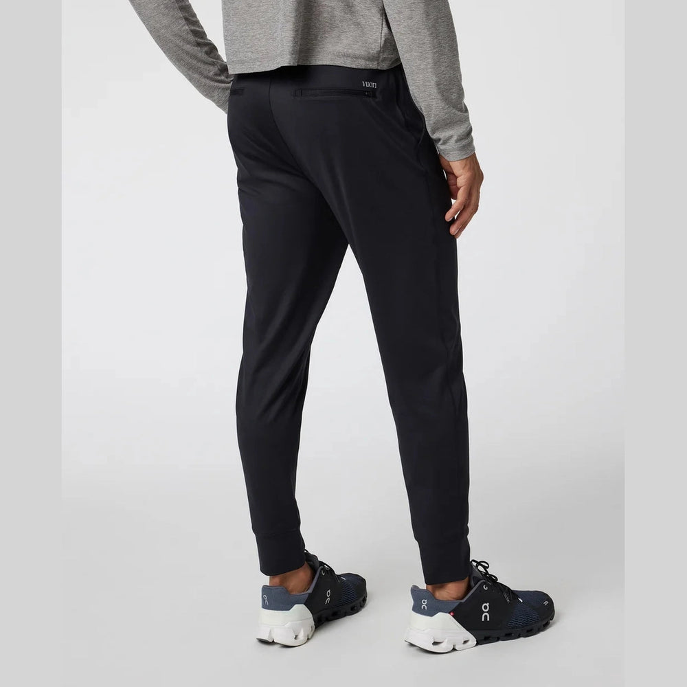 Person wearing black Vuori Sunday Performance Jogger – Men's pants and white sneakers on a light gray background