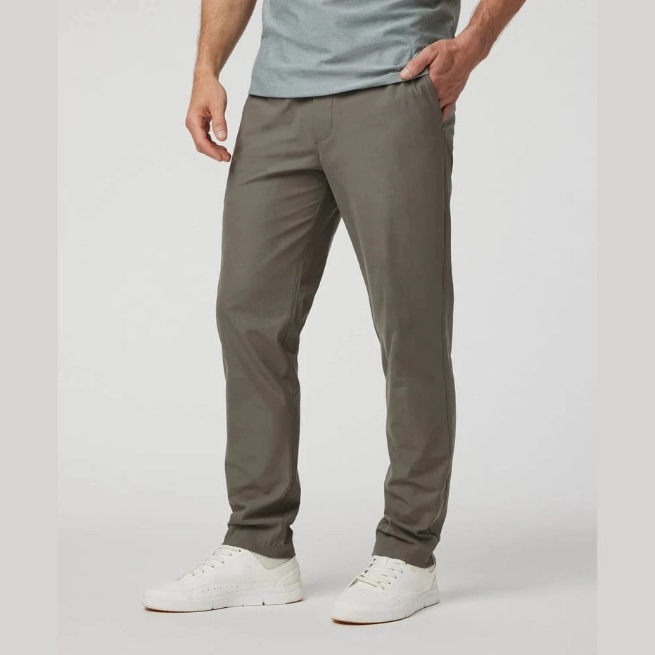 Person wearing olive green Vuori Meta Elastic Waist Pant – Men's pants and white shoes on a light gray background