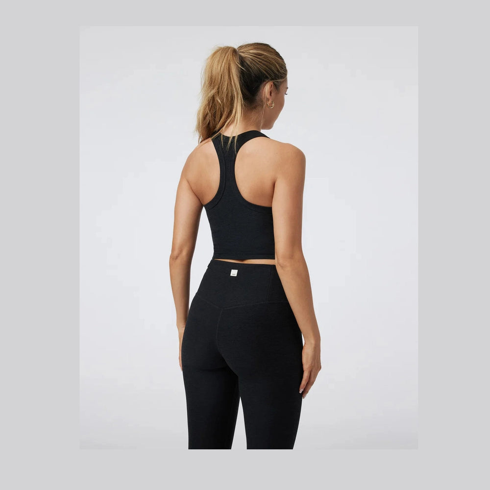 A woman shown from the back wearing a black Vuori Elevation Racer Bra – Women's athletic crop top and matching black leggings against a light gray studio background.