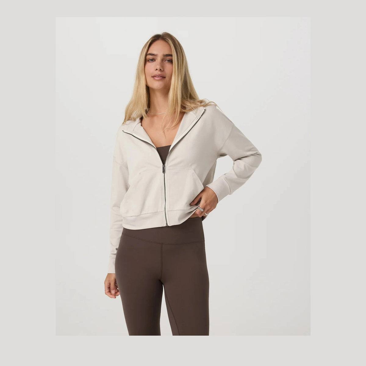 Woman wearing a beige Halo Modern Full Zip Hoodie – Women's and brown leggings on a white background