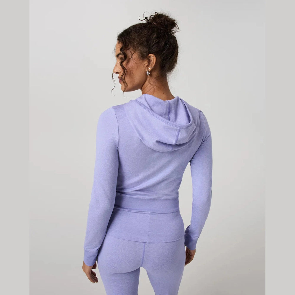 A woman shown from the back wearing a light lavender purple matching activewear set, consisting of a long-sleeve hooded top and high-waisted leggings, against a plain light gray studio background.