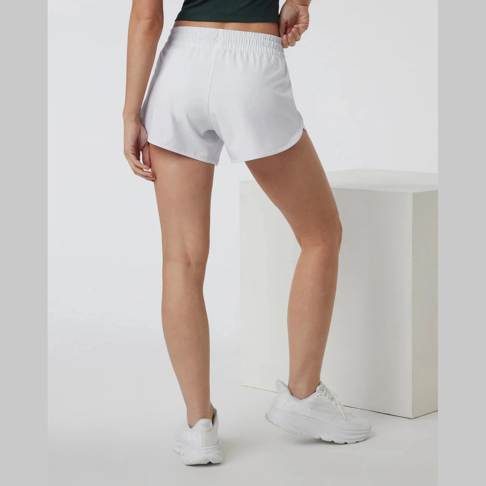 White Vuori Clementine 4" Short – Women's athletic shorts worn by a model, shown from the back in a studio setting with a white block prop.