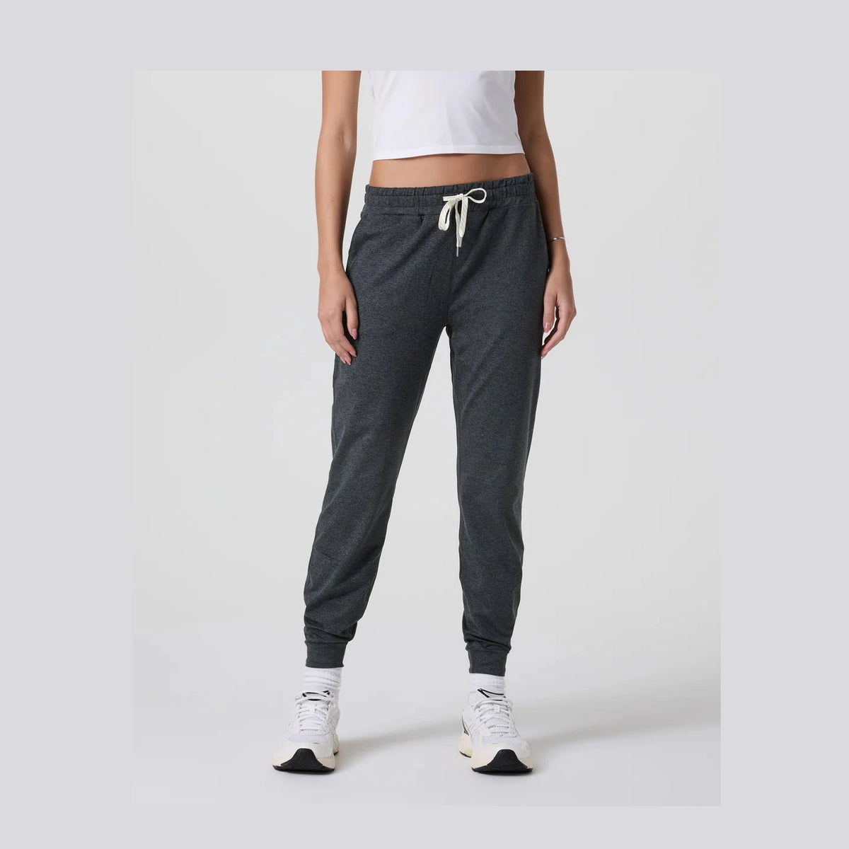 Person wearing dark gray Vuori Performance Jogger – Women's jogger pants and white sneakers on a light gray background