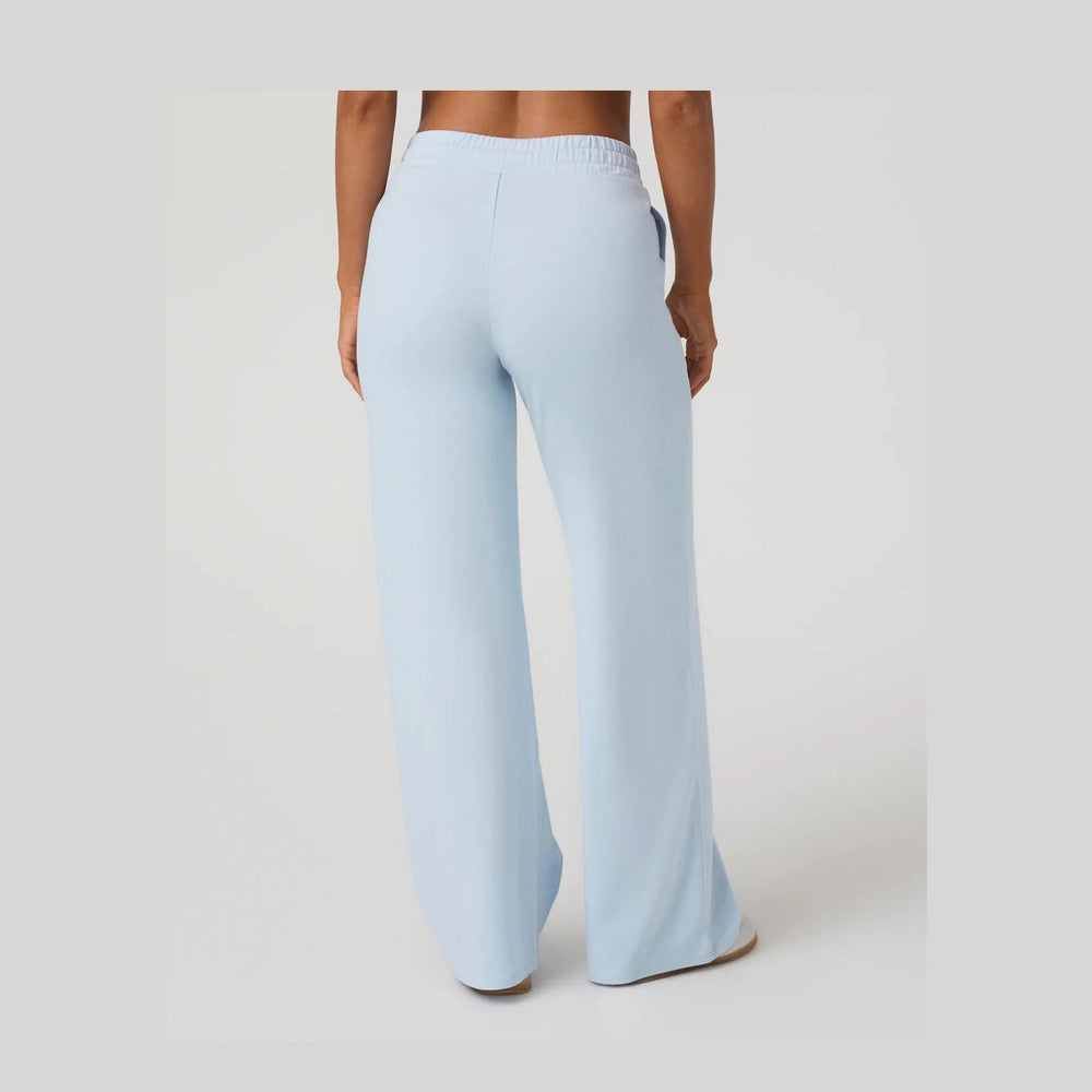 A person shown from the back wearing light blue wide-leg Vuori Halo Essential Wideleg – Women's pants against a plain light gray studio background.